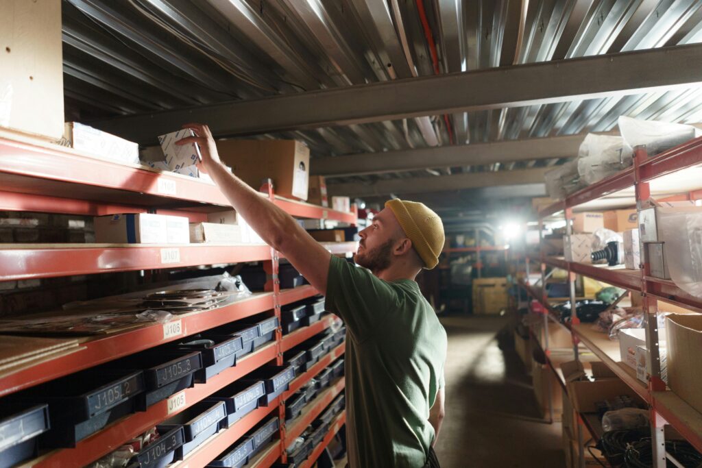 Man in green shirt and beige hat in middle of warehouse aisle collecting Just-in-Case inventory