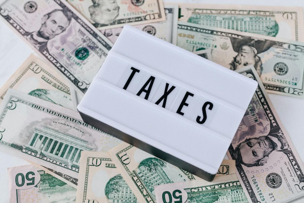 A plaque with the word "TAXES" spelled out in all uppercase letters over a pile of U.S. dollar notes ranging from $5 to $10 and $20 bills; this represents the automation capabilities of AI in Avalara sales tax software