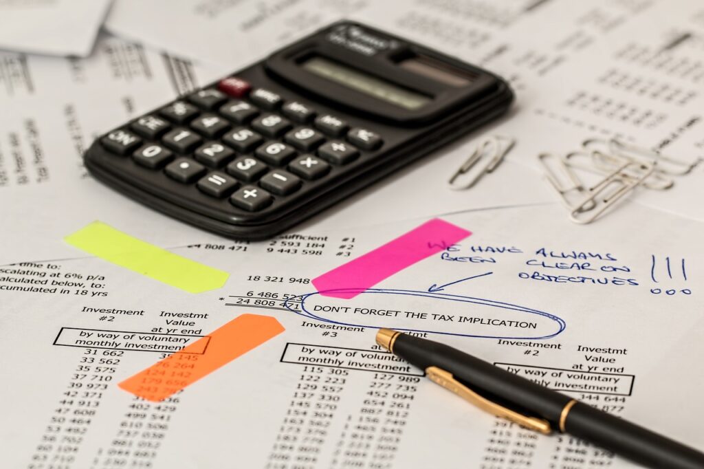 A calculater and pen on top of a paper spreadsheet being used to help maintain tax compliance instead of Avalara