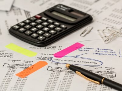 A calculater and pen on top of a paper spreadsheet being used to help maintain tax compliance instead of Avalara