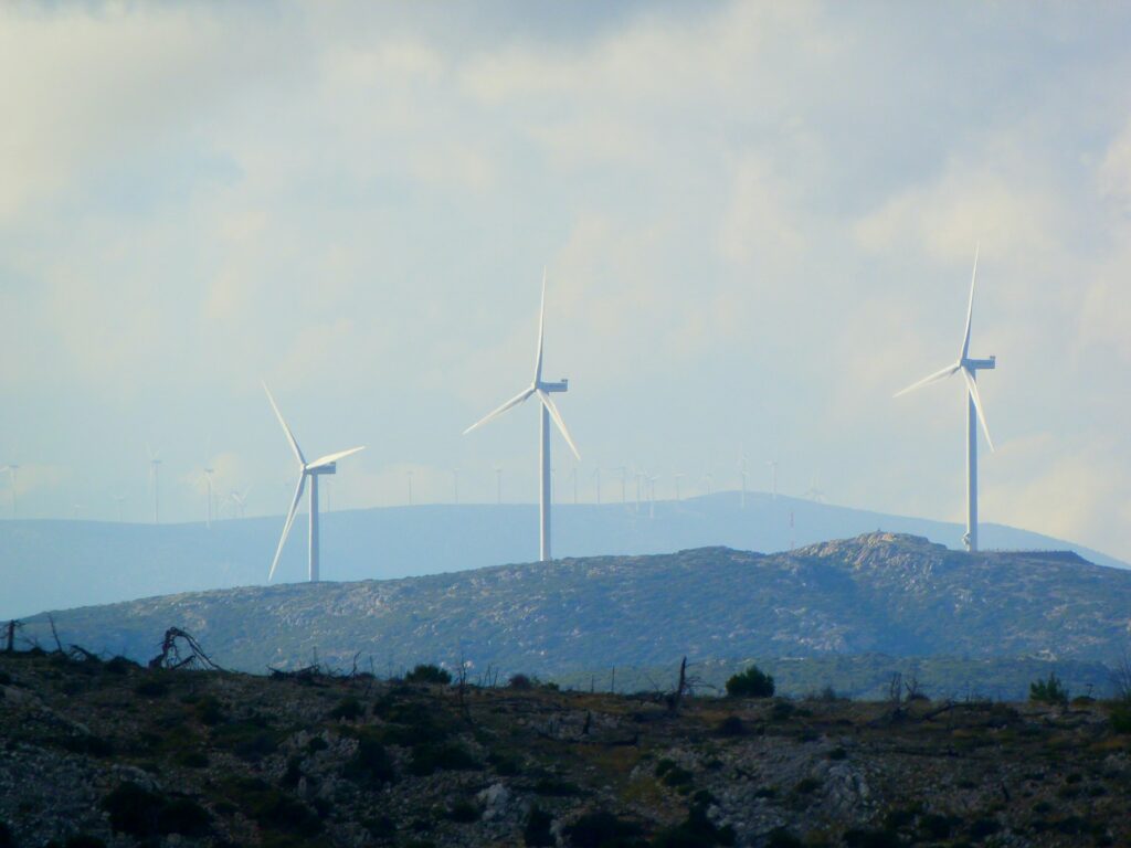 A skyline view over several green hills with three wind farm fans visible, in compliance with environmental, social and governance (ESG) demands