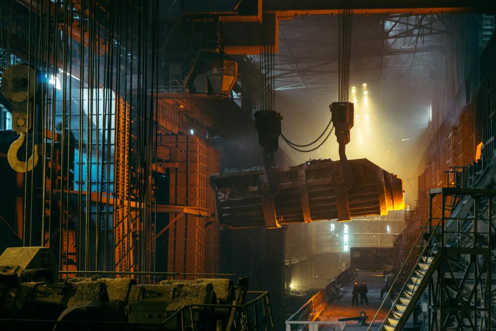 Dark manufacturing factory floor illuminated by orange and blue lighting, with steel production equipment and workers visible in the background, exemplifying production operations that could benefit from Acumatica Manufacturing Edition.