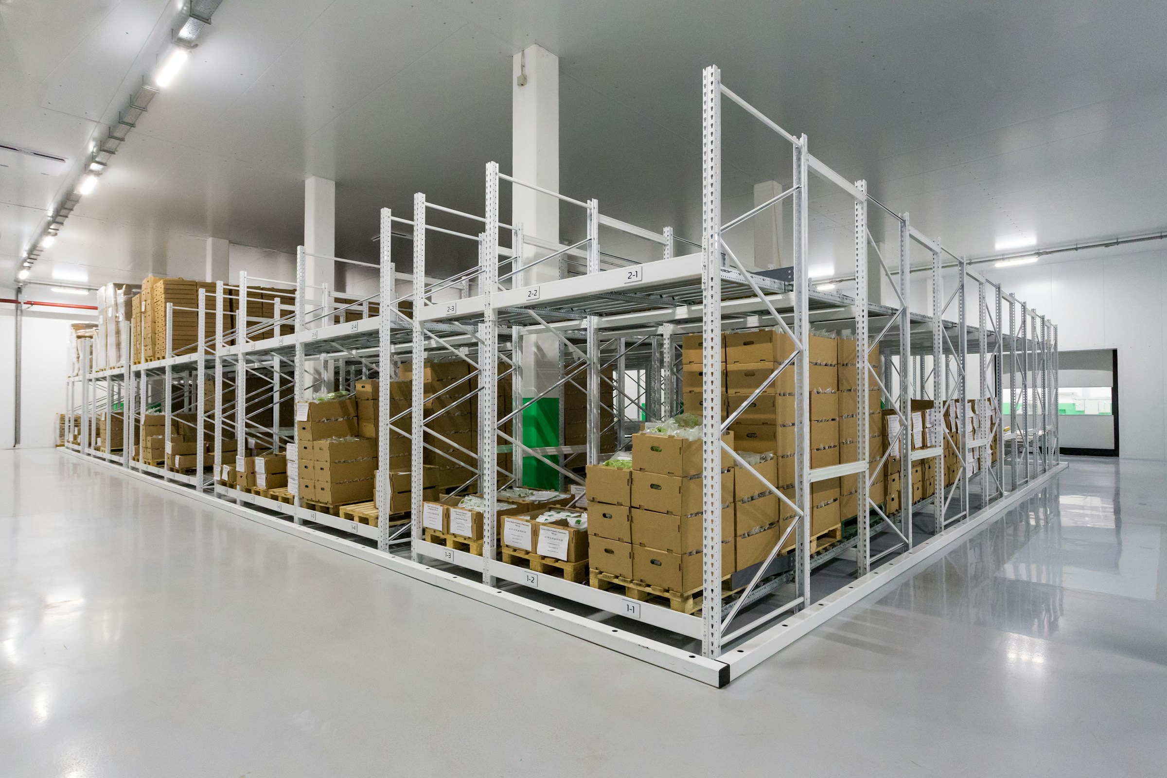 Industrial warehouse storage area with white metal pallet racking systems filled with cardboard boxes that are tracked by Savant WMS integrated with Acumatica ERP.