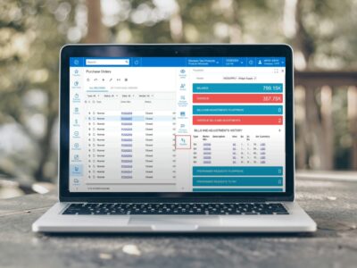 A laptop displaying purchase order reports in Acumatica with a side panel showing vendor payables and balance information against a blurred outdoor background.