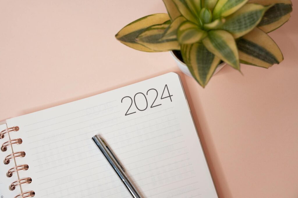 A notebook opened to a blank page marked "2024" with a pen placed across it, representing preparation for Sage 100 year-end closing procedures and tax reporting for the upcoming fiscal year.