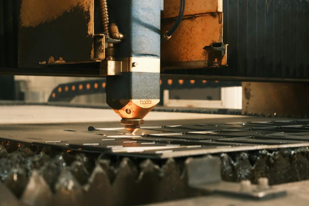 A close-up view of a laser cutting head in operation, showing the copper-colored nozzle cutting through metal with warm lighting highlighting the industrial machinery.