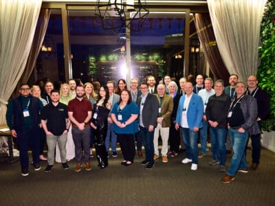 Group photo taken at La Cave in the Wynn Las Vegas during SWK Technologies' Customer Reception at Acumatica Summit 2025. Award recipients and SWK team members are gathered in front of an elegant venue entrance featuring white curtains and decorative greenery. Approximately twenty-five individuals are standing together in business casual attire, with the Venetian hotel visible through the windows in the background.