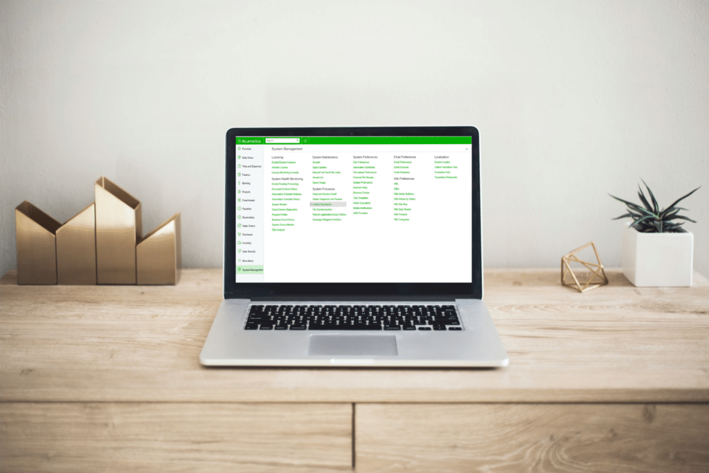 A MacBook laptop displaying the Acumatica ERP System Management interface on a wooden desk. 