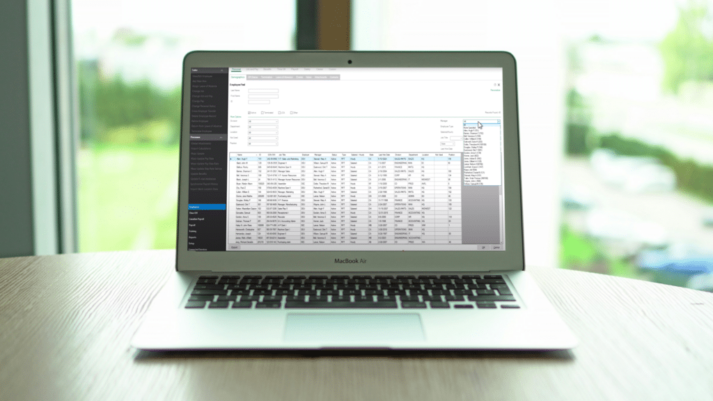 MacBook Air laptop displaying the Sage HRMS Employee Find interface with the More Options filtering panel expanded. The screen shows an employee list with detailed information including names, job titles, departments, and employment status for HR reporting purposes.